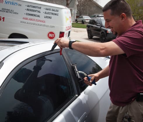 A technician opening a locked silver car with lockout tools, the company van parked behind